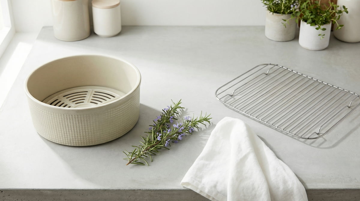 overhead view of ceramic air fryer basket and stainless steel rack on gray concrete counter with rosemary