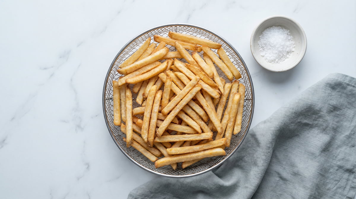 Crispy golden fries in an air fryer basket, showing the improved texture from preheating before cooking frozen foods