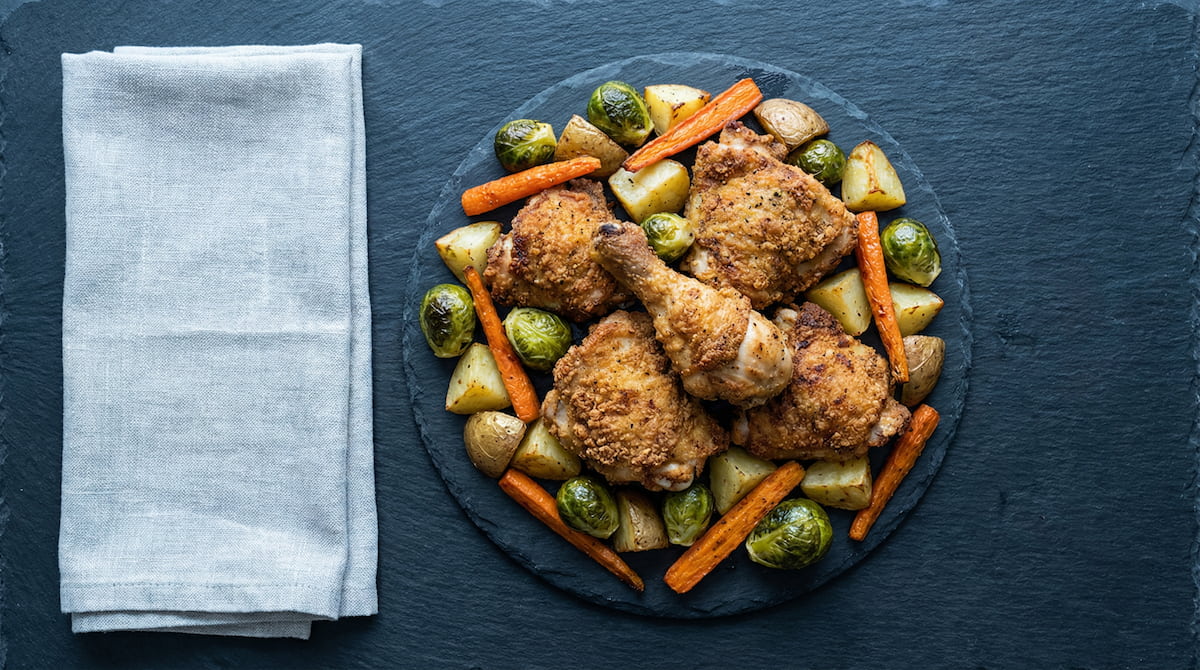 Air-fried chicken and vegetables on a dark surface, showing the crispy results of air fryer cooking compared to oven roasting