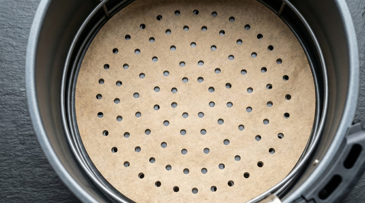 Perforated parchment paper liner inside an air fryer basket — the holes allow air circulation for crispier results