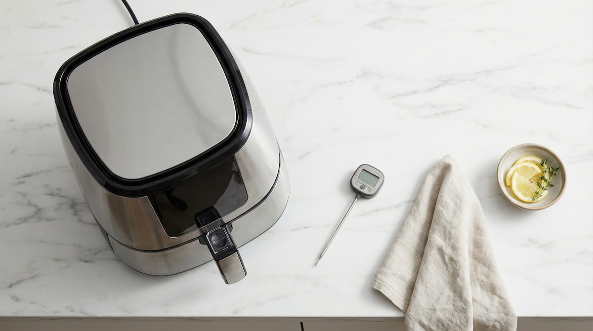 Air fryer and kitchen thermometer on white marble counter showing temperature measurement concept