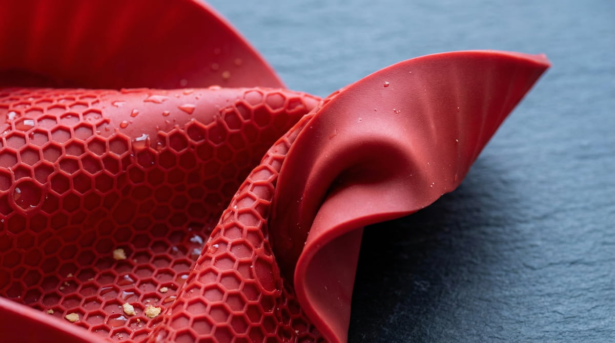 Close-up of a red silicone air fryer liner twisted to check material quality — cheap fillers show white when bent