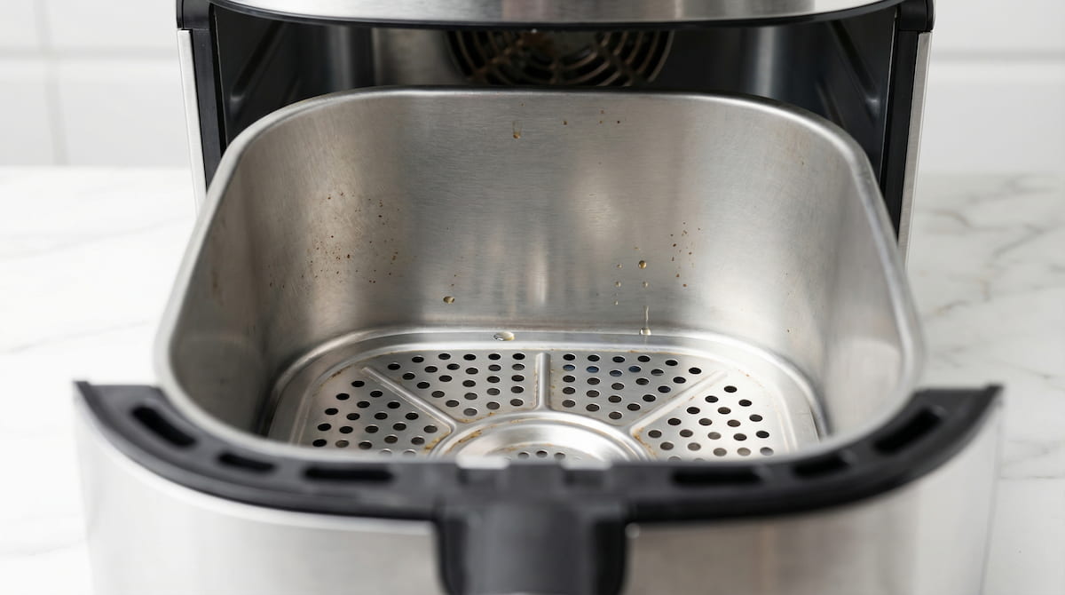 macro close-up of stainless steel air fryer interior cooking surface on white marble background