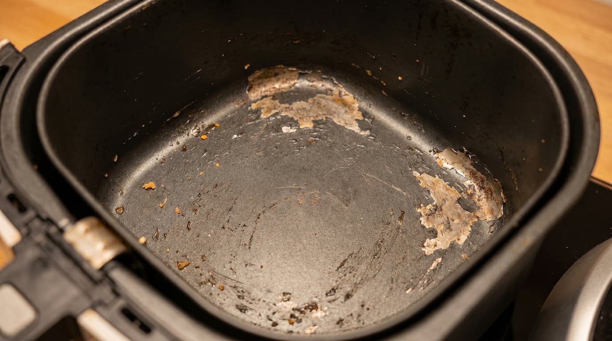 Worn air fryer basket with peeling nonstick coating near the corners