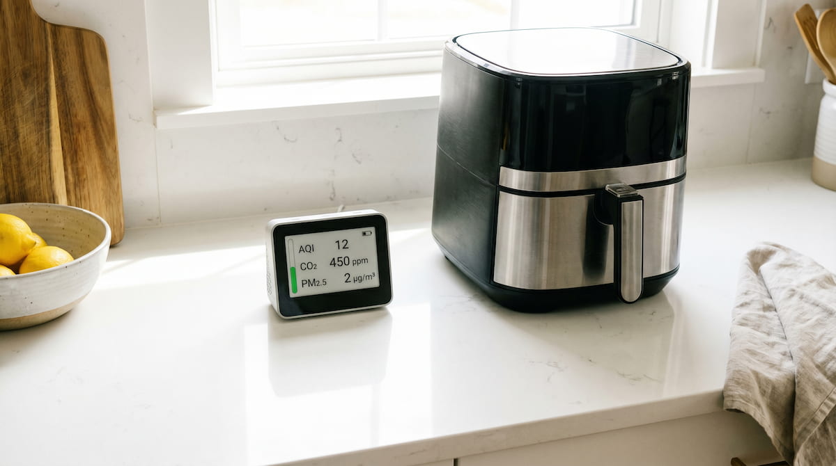 indoor air quality monitor placed next to air fryer on kitchen counter